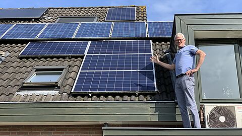 energieambassadeur Ad van Rooijen naast de zonnepanelen op zijn dak 